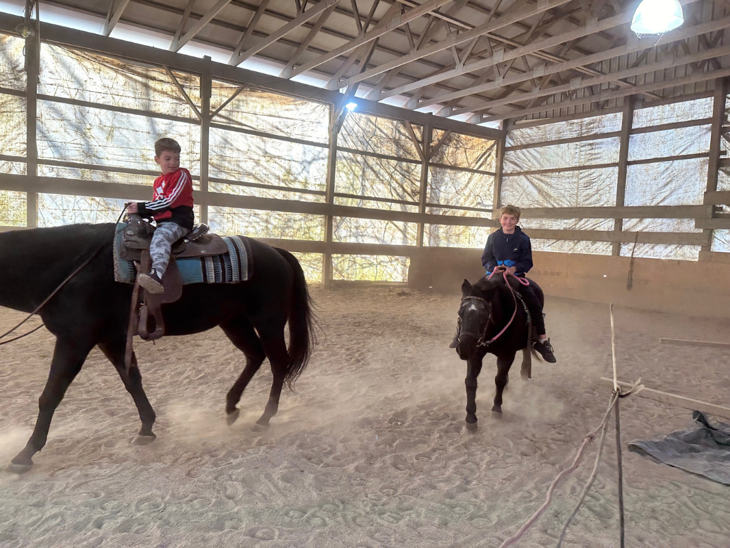 Two young riders on horseback in an indoor arena