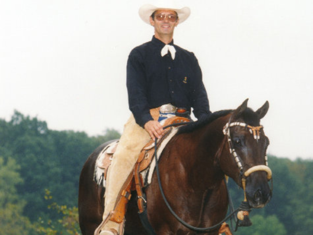 A man wearing a cowboy hat rides a horse across an open landscape, showcasing a classic Western scene.