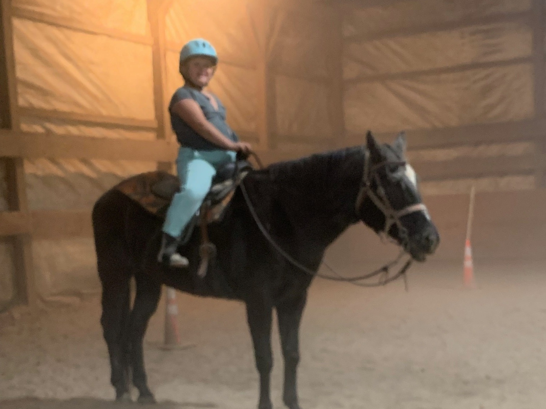 Inside an indoor arena, a woman confidently rides a horse